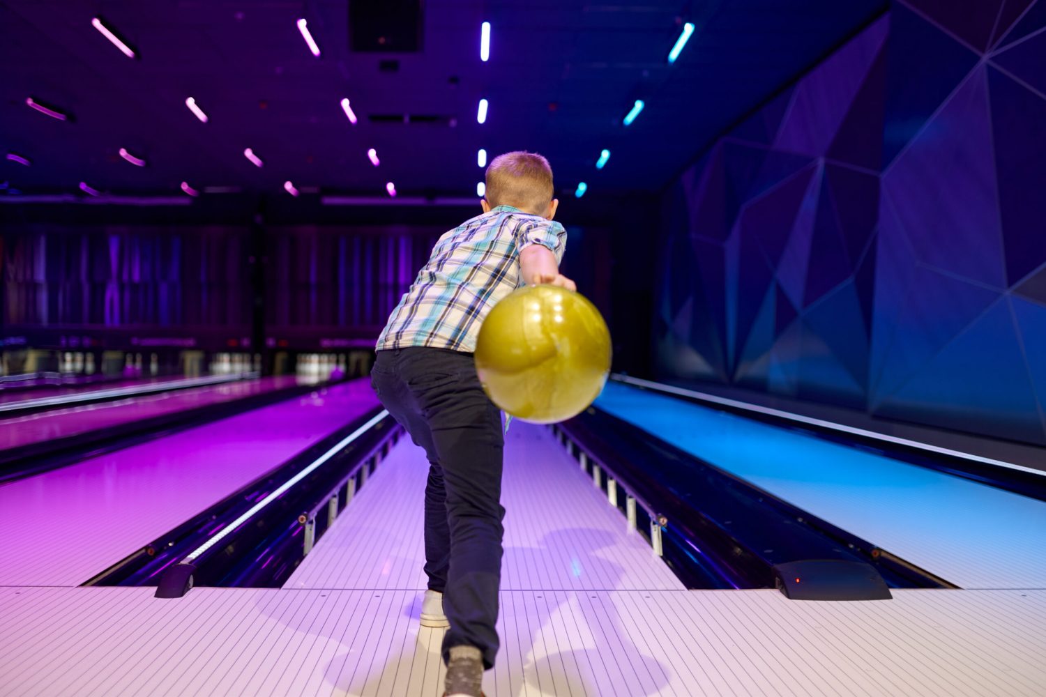 Boy holds a ball at the lane in bowling alley. Kid preparing to score a strike. Children having fun in entertainment center, bowler kid